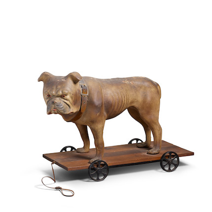 A PAPIER MACHE BULLDOG PULL TOY circa 1900, with wood base and cast-iron wheelsheight 15 1/2in (39.5cm); length 24in (61cm); width 10 1/2in (27cm) image 1